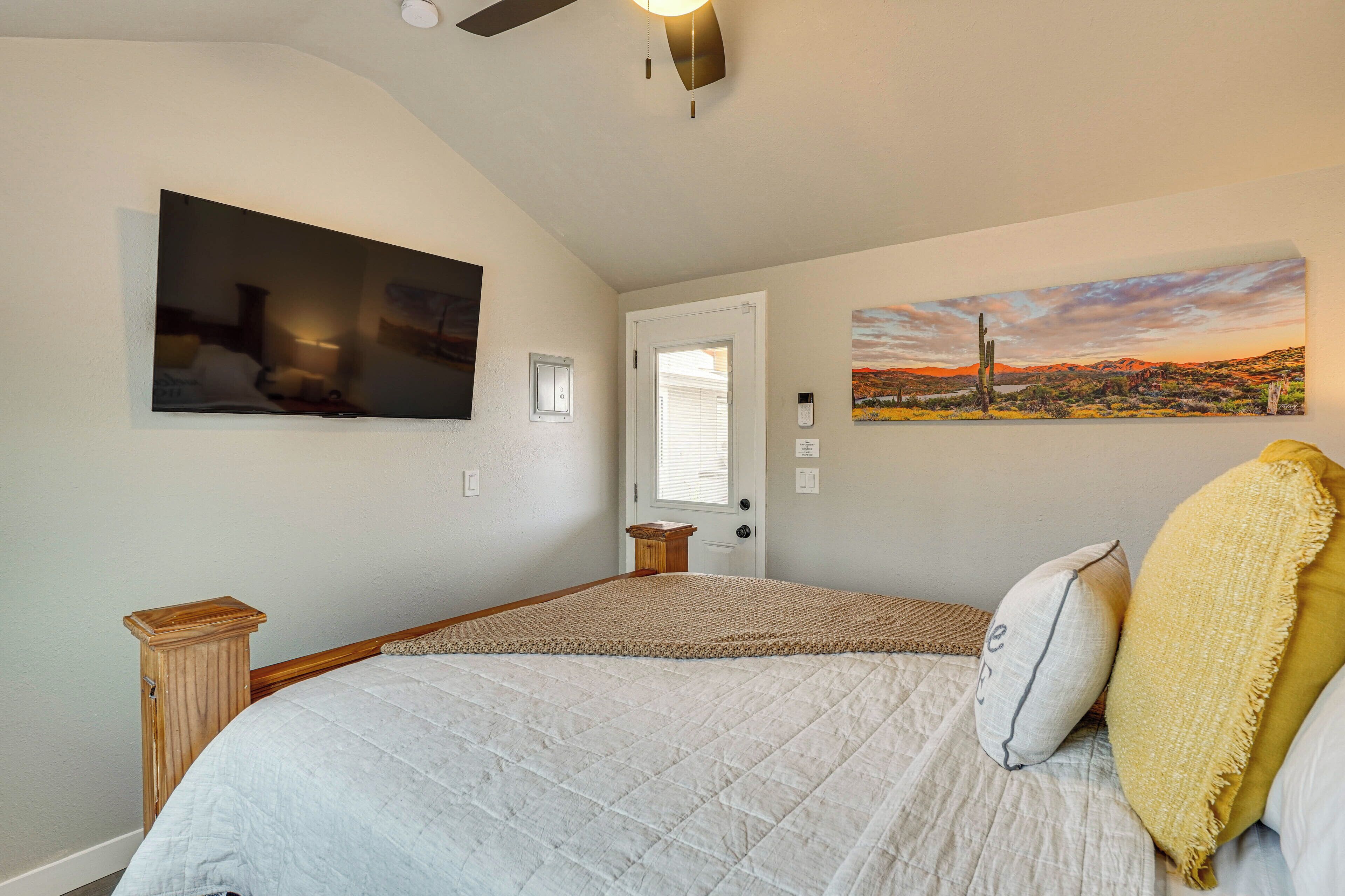 Quarto com cama, ventilador de teto, porta e duas pinturas penduradas na parede.