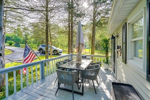 A covered porch with a table and chairs, a flag, and a car parked in the background. - Fire Pit, Deck & Water Views: Athens Home! (Athens)