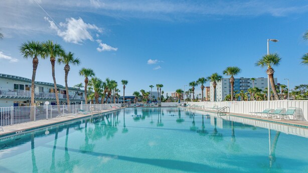 A swimming pool with clear blue water, surrounded by palm trees and lounge chairs. - Walk to Indian Shores Beach + Pool: Sunny Condo (Indian Shores)