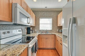 A kitchen with wooden cabinets, a microwave, stove, oven, sink, and a refrigerator. - Walk to Indian Shores Beach + Pool: Sunny Condo (Indian Shores)