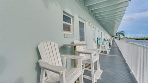 A covered outdoor area with white Adirondack chairs and tables, a white railing, and a view of the ocean. - Walk to Indian Shores Beach + Pool: Sunny Condo (Indian Shores)