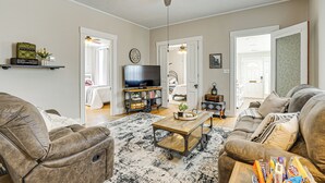 A living room with a ceiling fan, a television, a sofa, a coffee table, and a bookshelf. - Dog-friendly Home w/ Yard, 6 Mi to Louisville! (New Albany)