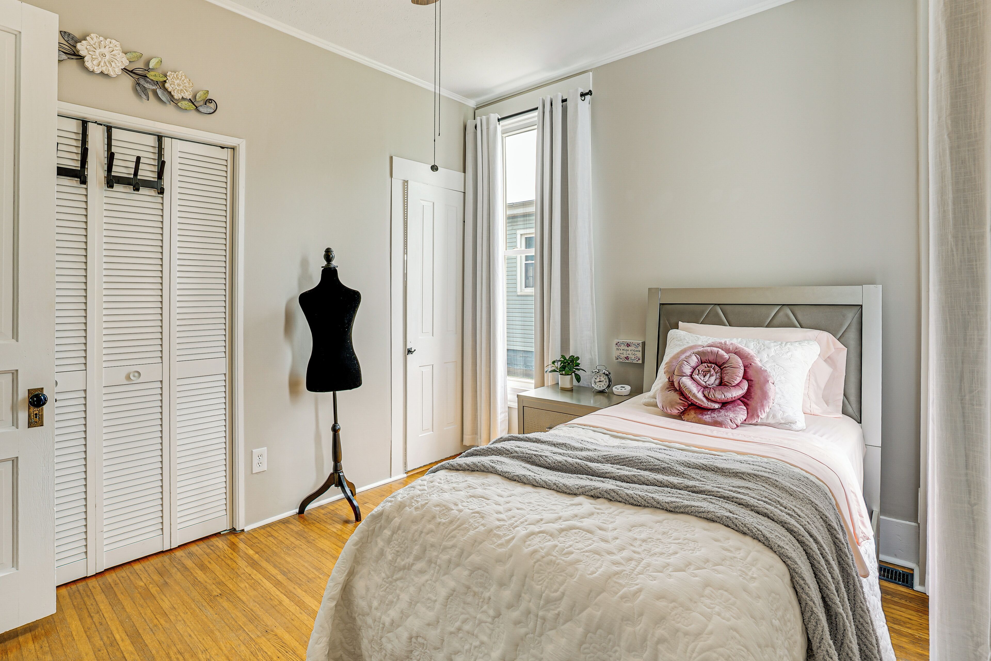 A bedroom with a bed, a dresser, a mannequin, and a window with curtains.