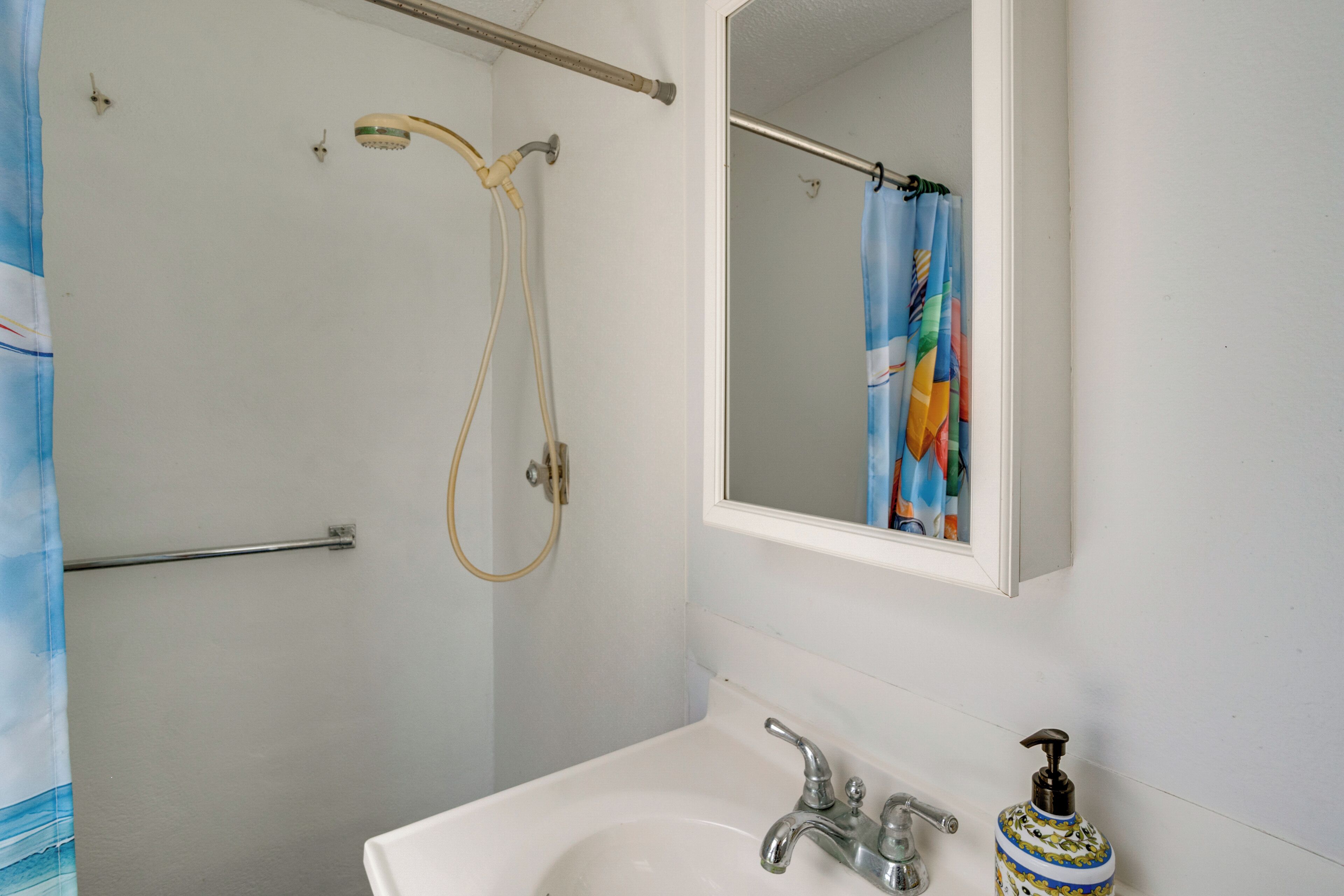 A bathroom with a shower, a sink, a mirror, and a soap dispenser.