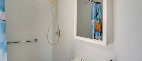 A bathroom with a shower, a sink, a mirror, and a soap dispenser.