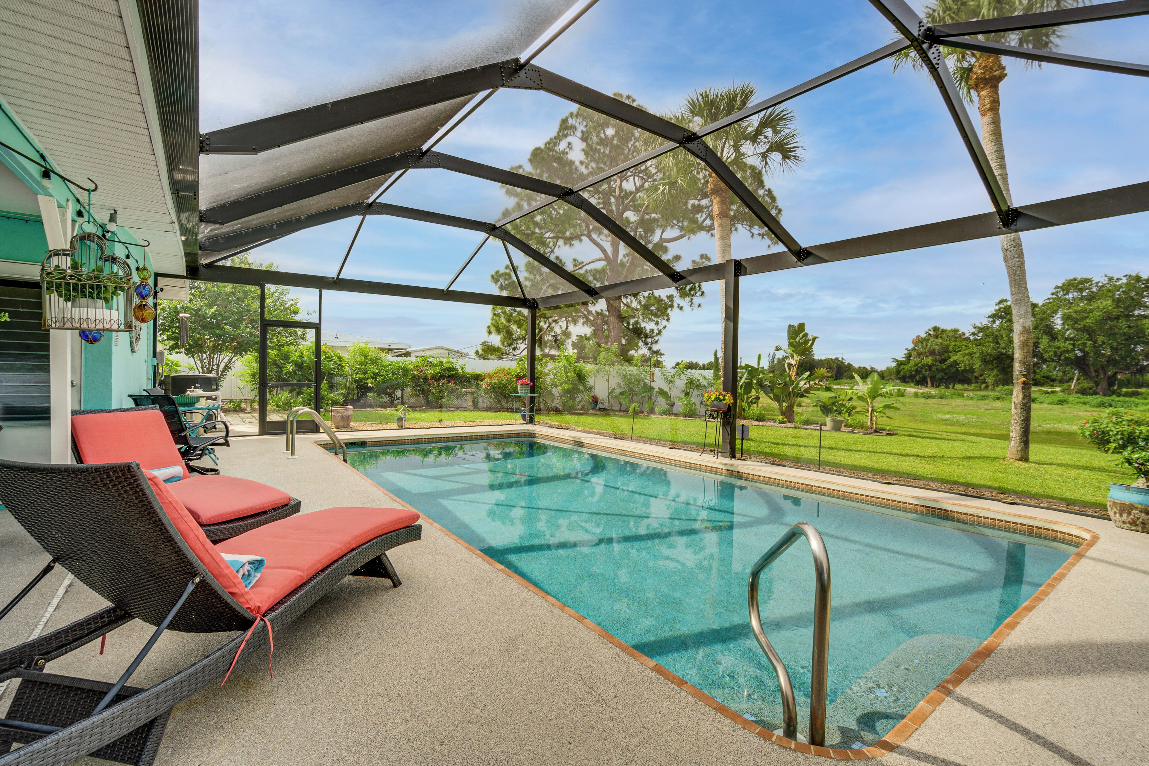 A covered outdoor swimming pool with lounge chairs, a pergola, and a view of the surrounding greenery.