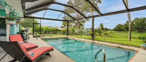 A covered outdoor swimming pool with lounge chairs, a pergola, and a view of the surrounding greenery.