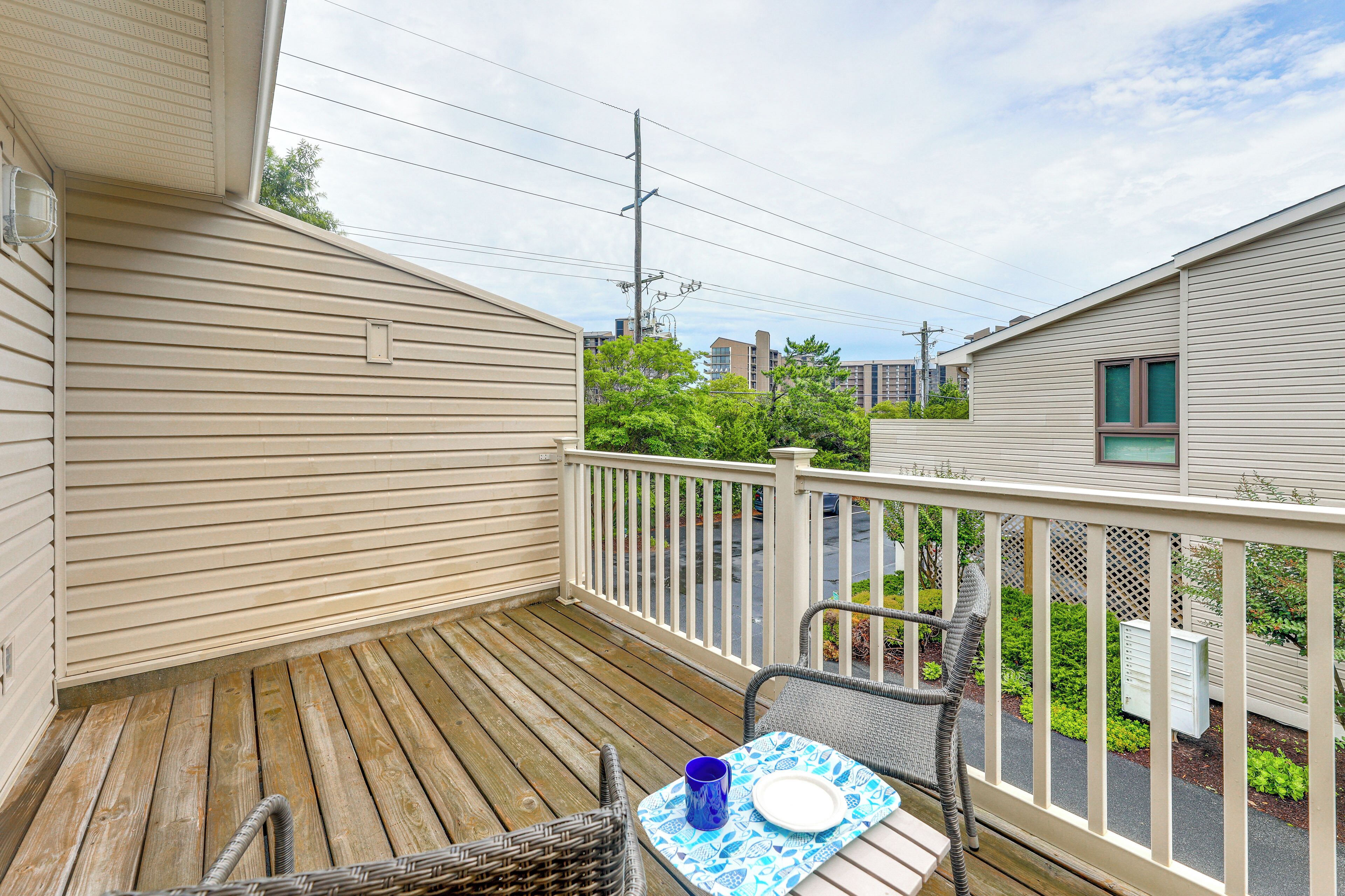 Une terrasse en bois avec une table et des chaises, une rambarde et une vue sur les bâtiments voisins.