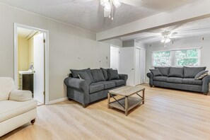 Een ruime woonkamer met twee grijze banken, een houten salontafel en houten vloeren.