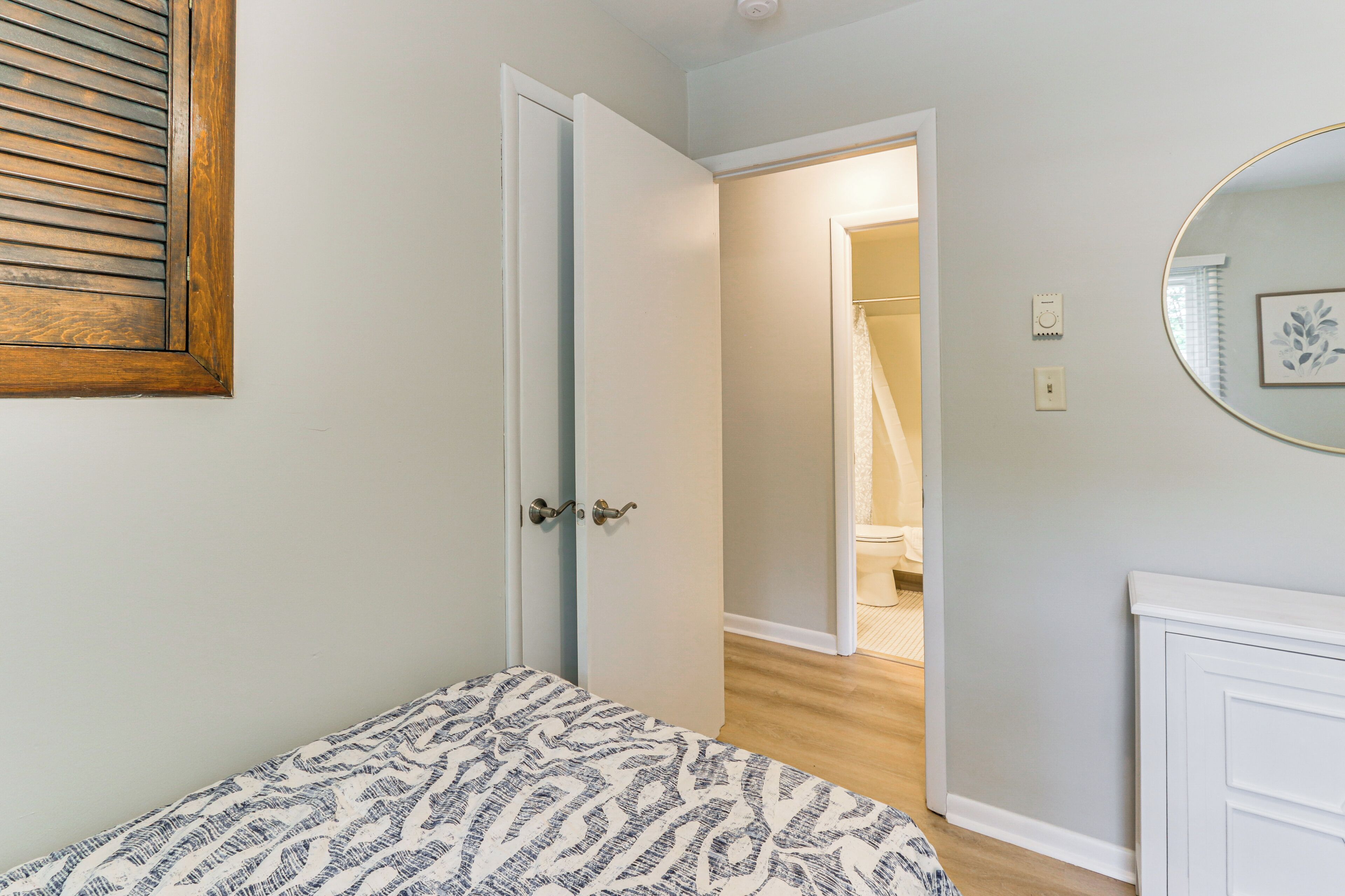 Une chambre à coucher avec un lit, une porte donnant sur une salle de bain et un miroir au mur.