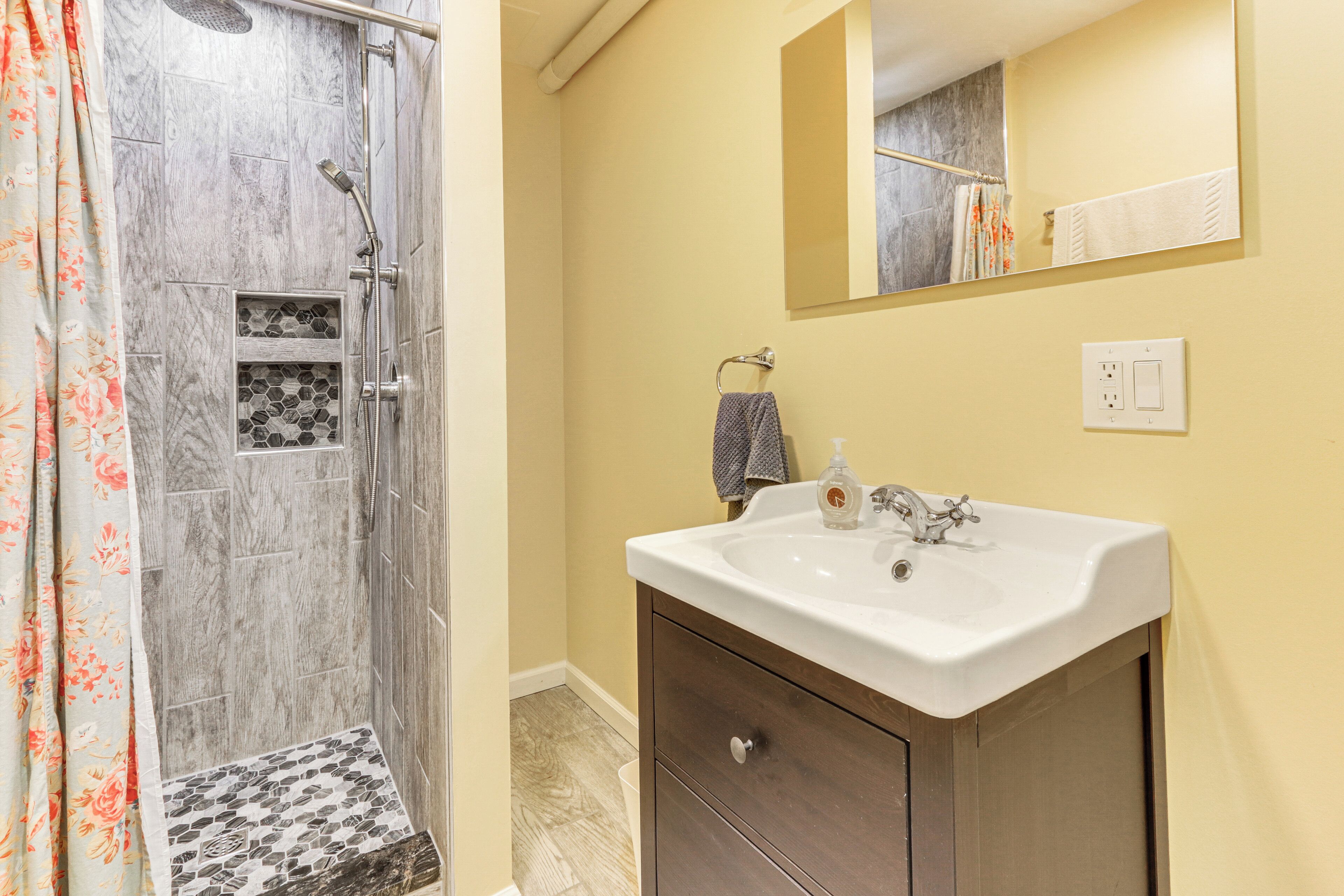 A bathroom with a shower, a sink, a mirror, and a towel rack.