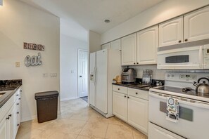 A kitchen with white cabinets, a refrigerator, a microwave, and a stove. There is a trash can and a kitchen sign on the wall. - Sunny Sarasota Stay: Screened Pool + Pet Friendly (Sarasota)