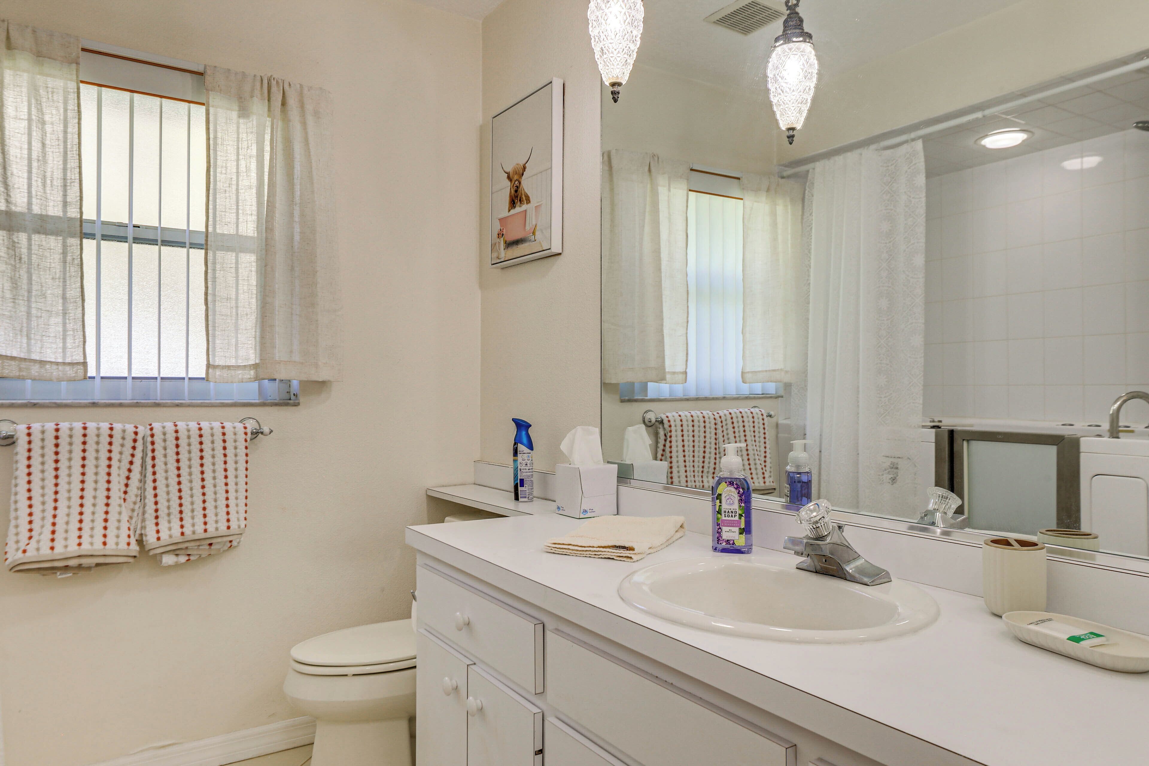 A bathroom with a white sink, mirror, and toilet. There are towels hanging on the wall and a window with curtains.