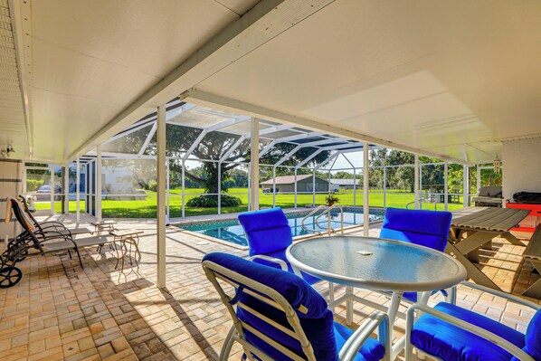 A covered outdoor area with a pool, blue chairs, and a table. - Sunny Sarasota Stay: Screened Pool + Pet Friendly (Sarasota)