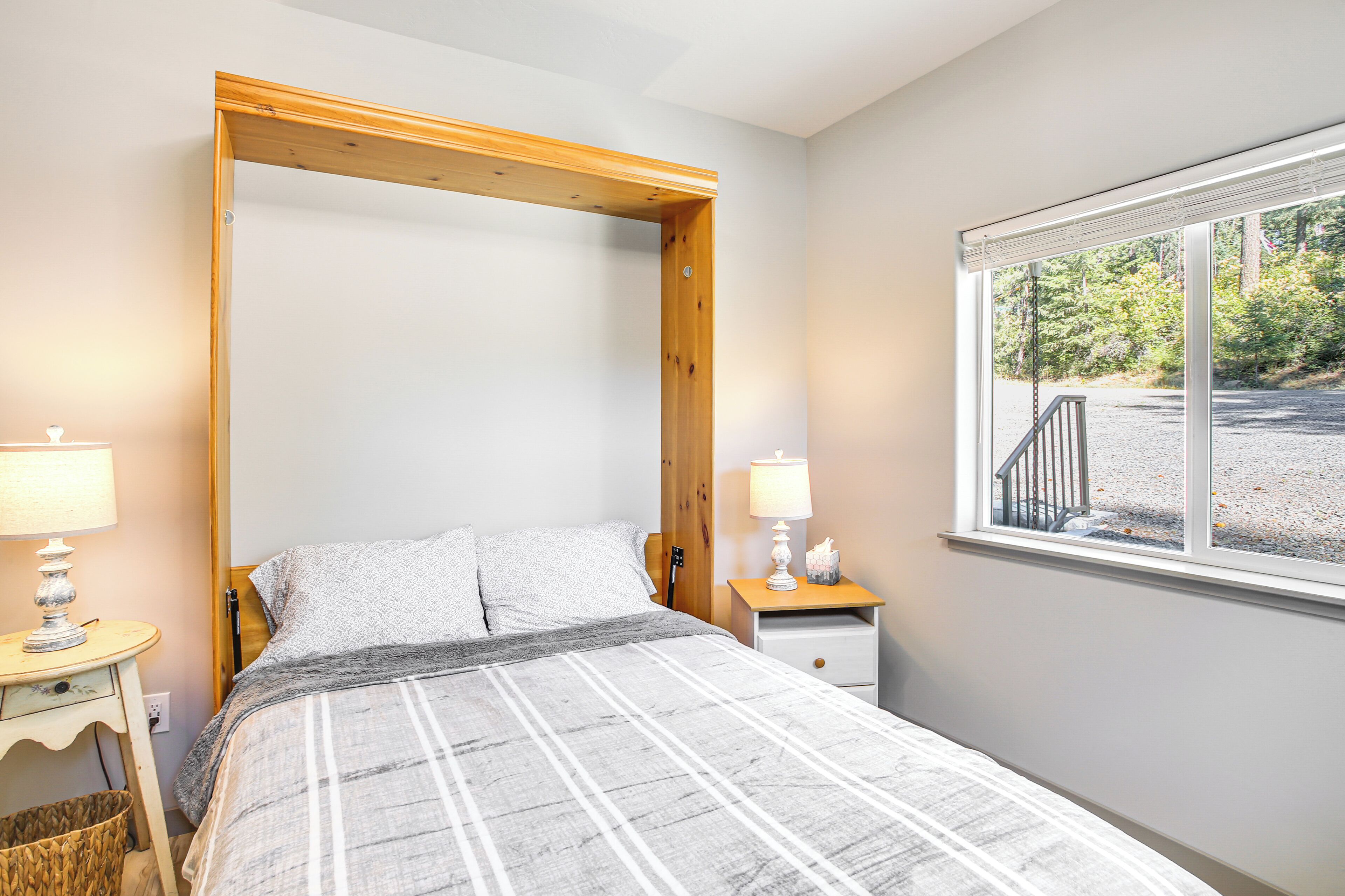 A bedroom with a bed, two bedside tables, a window with a view of trees, and a wooden headboard.