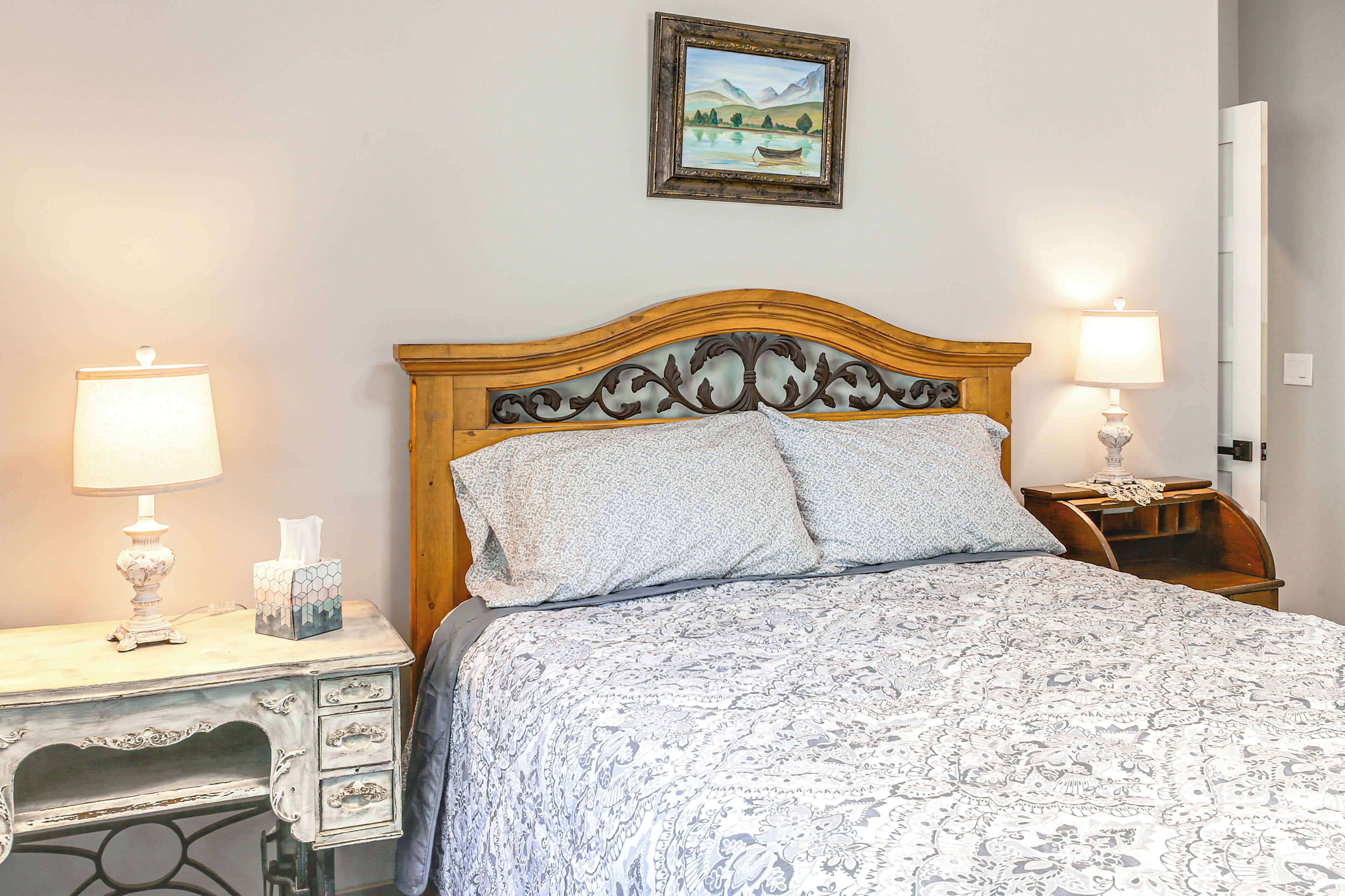 A neatly made bed with a patterned bedspread, a wooden headboard, and two bedside lamps.