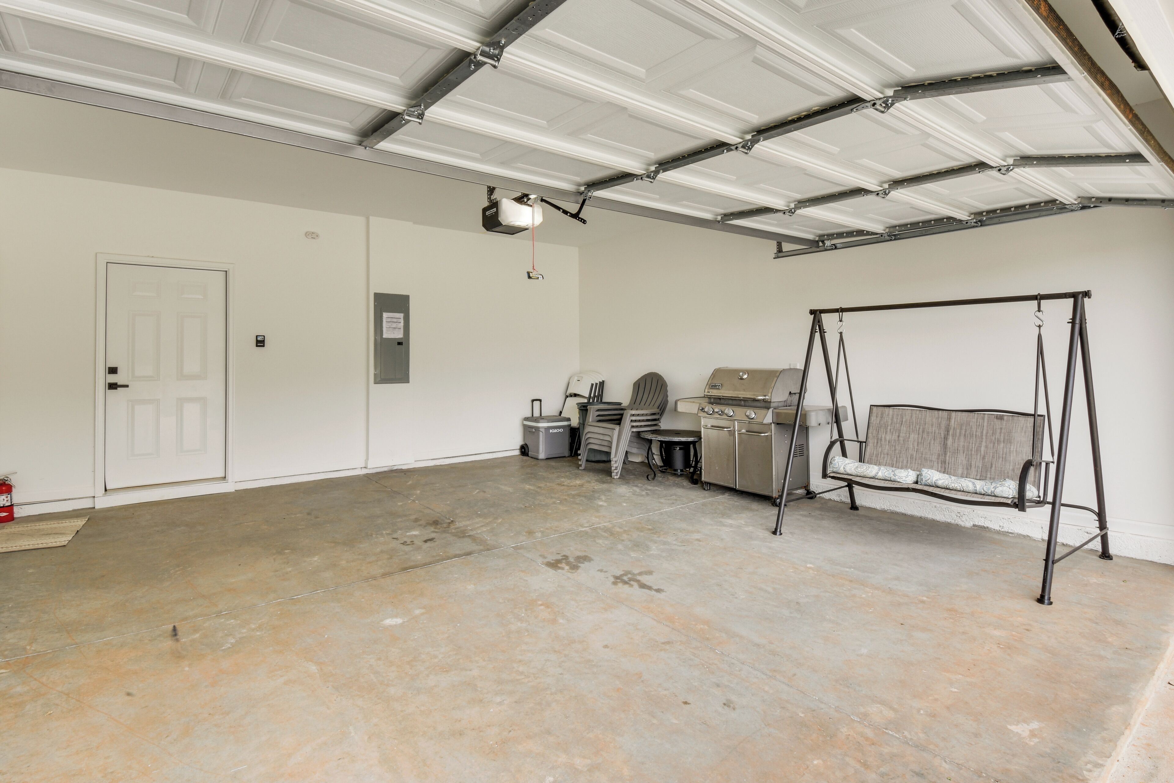 A garage with a white door, a bench, a projector, and a ceiling with exposed beams.