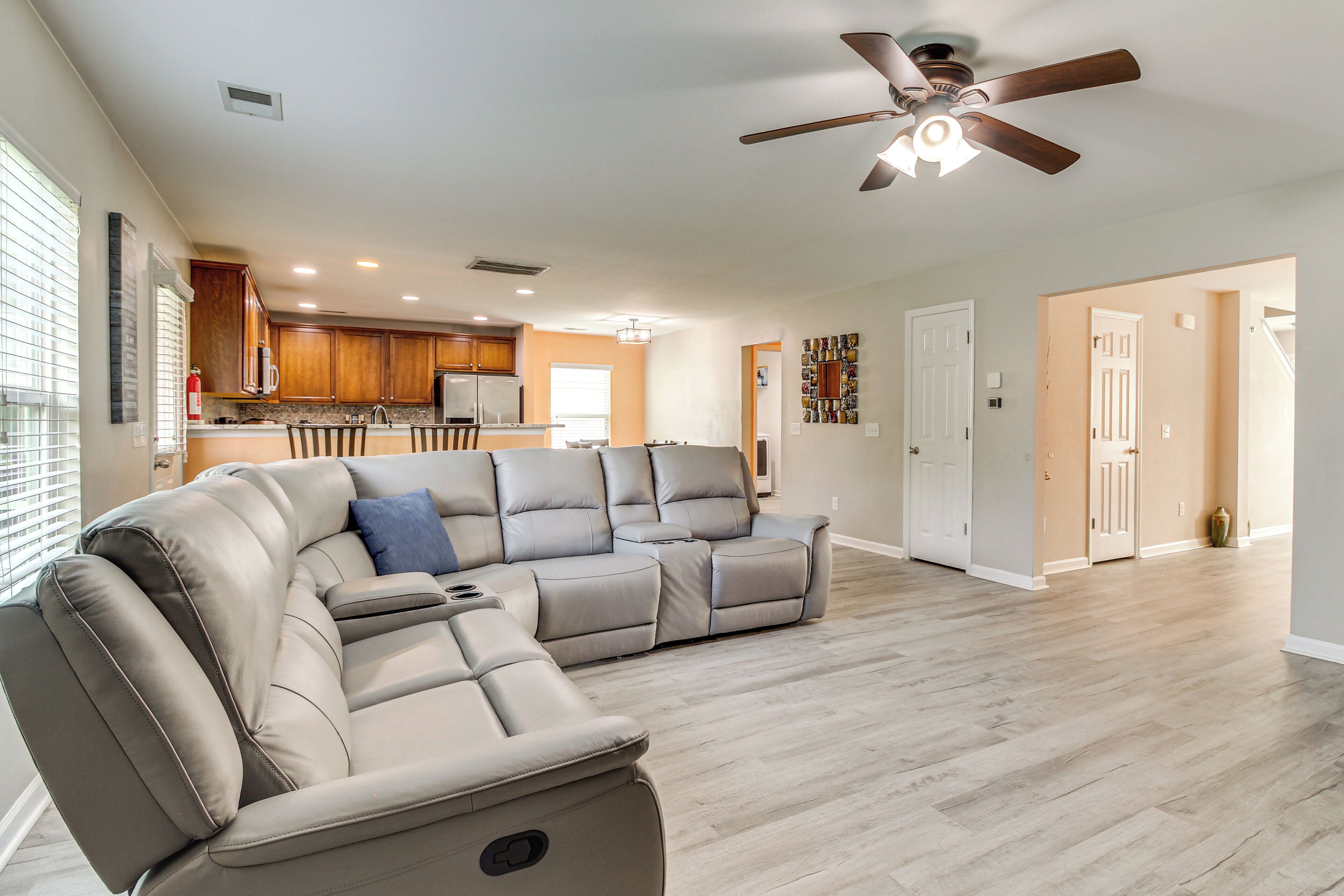 A spacious living area with a large sectional sofa, a ceiling fan, and a kitchen in the background.
