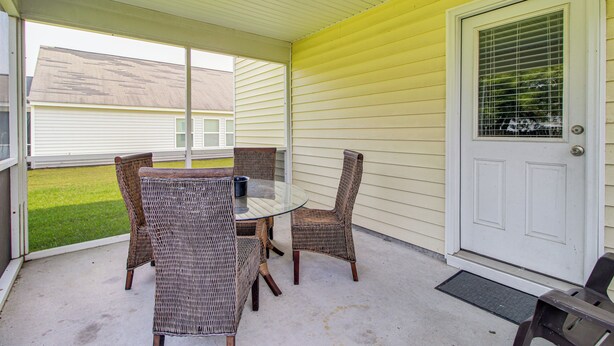 A covered patio with wicker furniture and a white door. - Spacious Home w/ Screened Patio in Pooler! (Pooler)