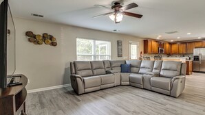 A modern living room with a sectional sofa, a ceiling fan, and a kitchen in the background. - Spacious Home w/ Screened Patio in Pooler! (Pooler)