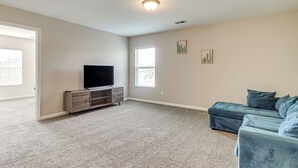 A living room with a flat-screen TV, a gray carpet, a blue sofa, and a wooden entertainment center. - Spacious Home w/ Screened Patio in Pooler! (Pooler)