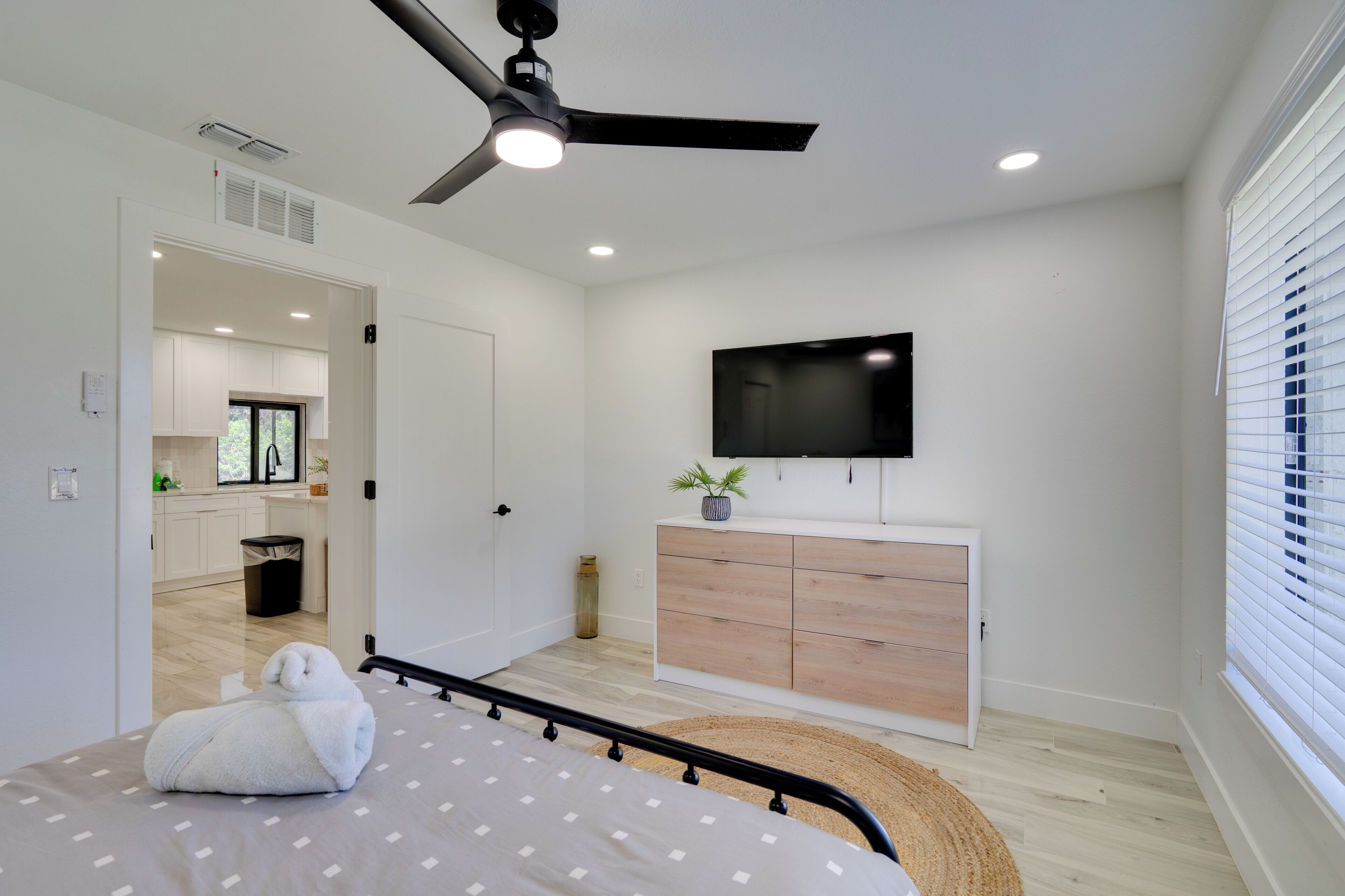 Une chambre moderne équipée d’un lit, d’un ventilateur de plafond, d’une télévision et offrant une vue sur la cuisine et la salle de bain.