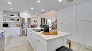 Una cocina moderna con armarios blancos, electrodomésticos de acero inoxidable y una isla central con una cesta y flores.