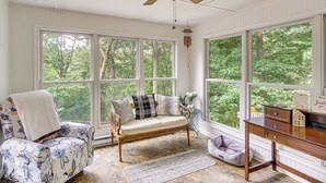 Una habitación acogedora con sofá de madera, un escritorio y ventanas amplias con vistas a árboles.