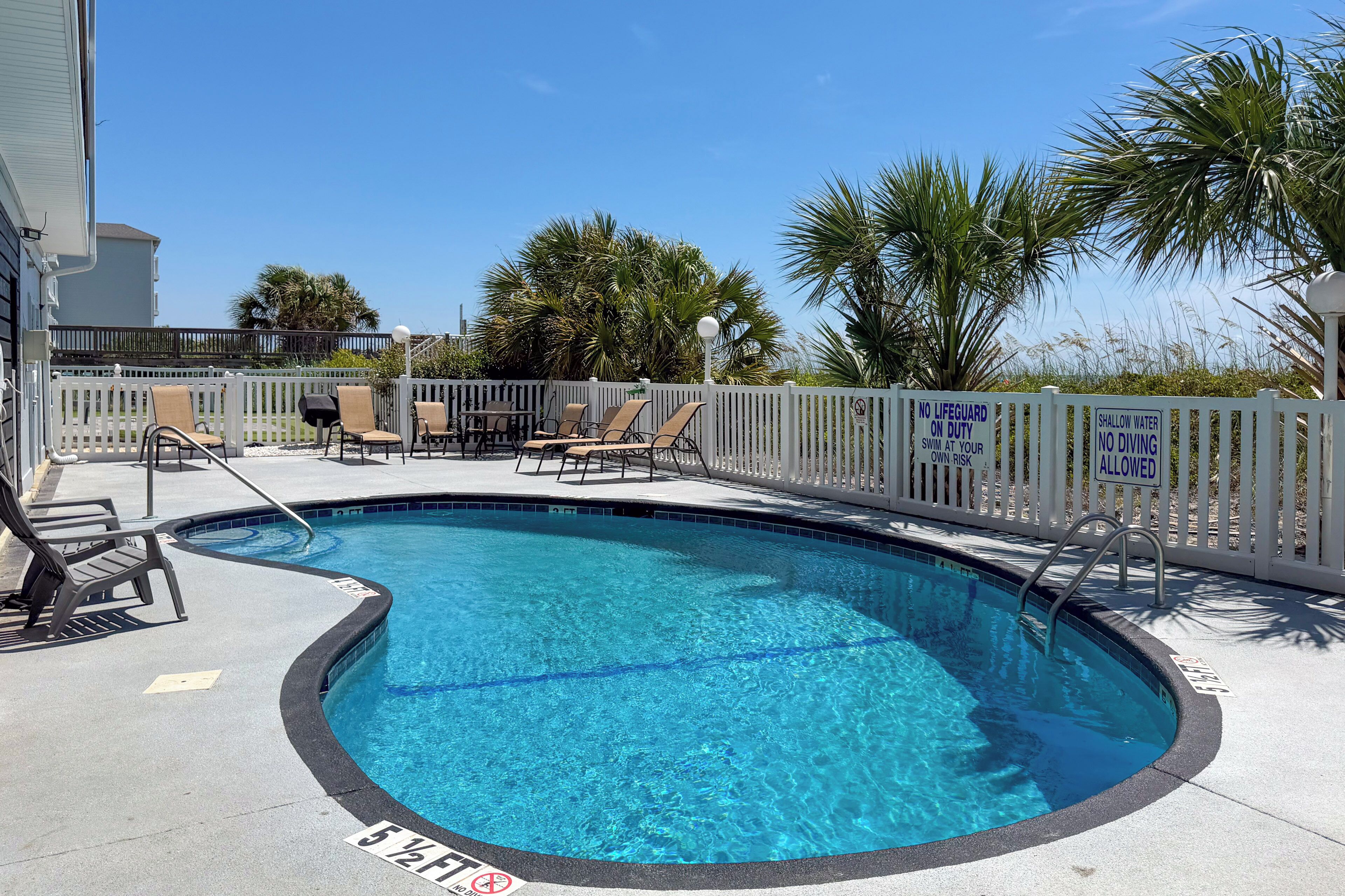 A swimming pool with lounge chairs and a white fence.