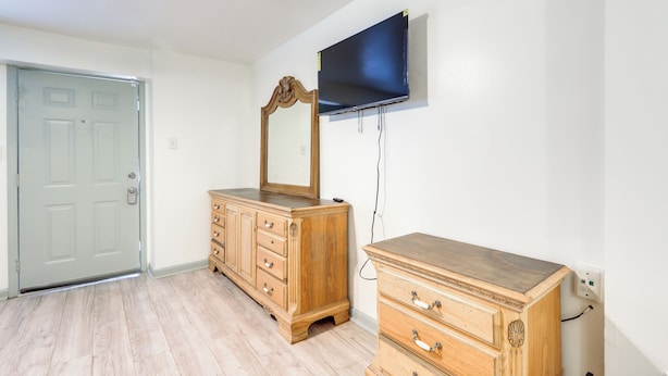 A room with a wooden dresser, a mirror, and a flat-screen TV mounted on the wall. - Easy Highway Access: Low-key Norcross Studio! (Norcross)