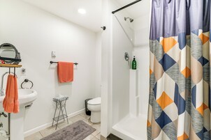 Un baño con lavamanos blanco, espejo e inodoro. Hay una cortina de ducha con un diseño geométrico.