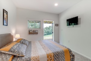 A bedroom with a bed, a TV mounted on the wall, a window, and a door leading outside.