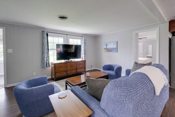A living room with a television, blue upholstered furniture, a wooden coffee table, and a painting on the wall.