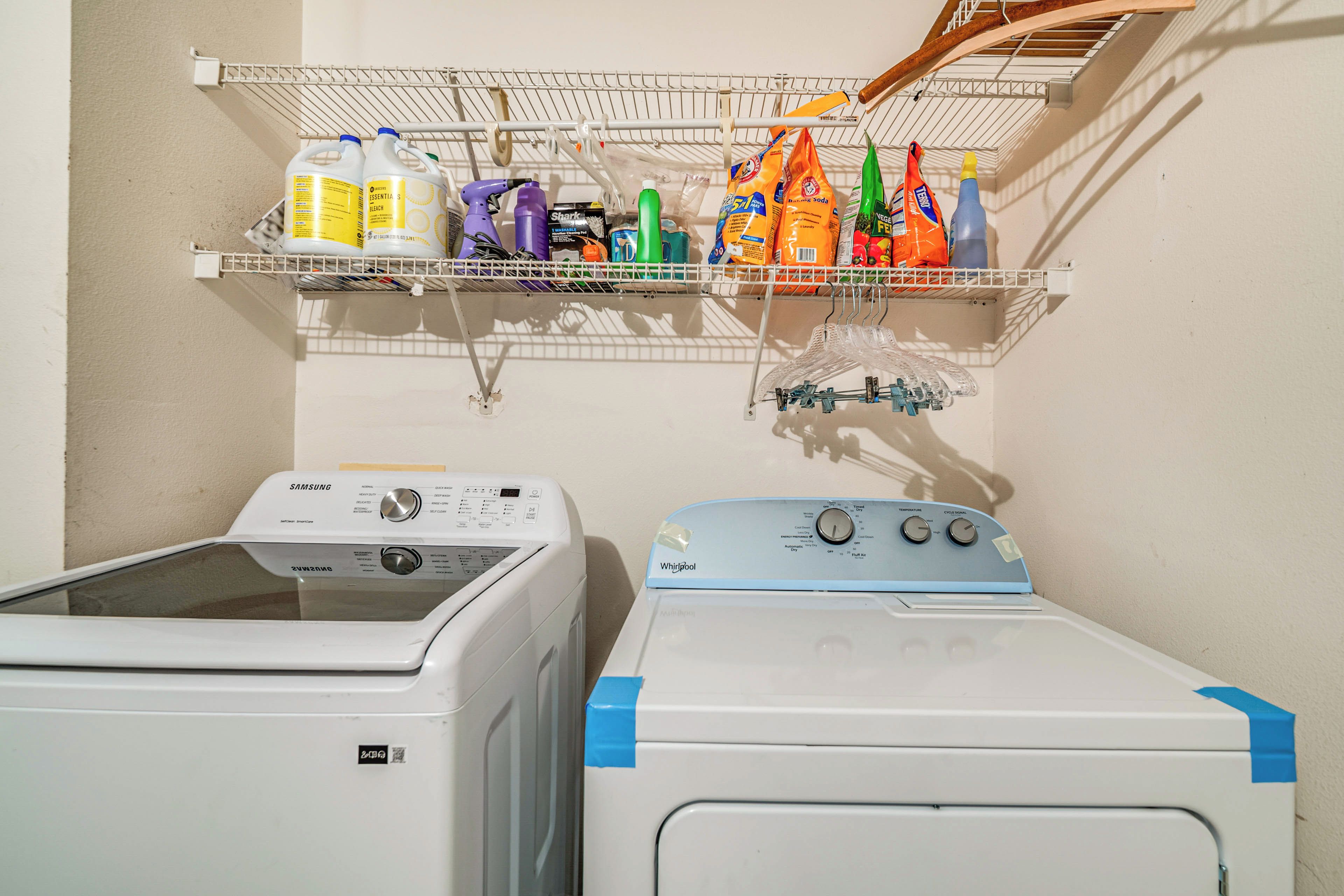 A laundry area with two washing machines and a shelf above containing cleaning supplies.