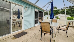 A covered patio with a table and chairs, a blue umbrella, and a sliding glass door leading to an outdoor seating area. - 2BR Pet-friendly Vacation Rental The Villages! (Lady Lake)