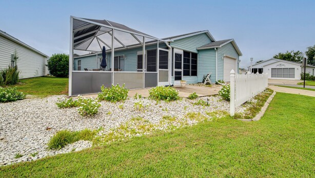 A single-story house with a covered patio area, a front yard with a gravel pathway, and a white picket fence. - 2BR Pet-friendly Vacation Rental The Villages! (Lady Lake)
