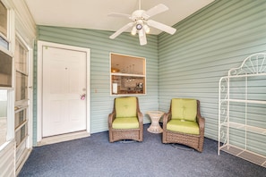 A room with two wicker chairs with green cushions, a ceiling fan, a white door, and a window with a view of a kitchen. - 2BR Pet-friendly Vacation Rental The Villages! (Lady Lake)