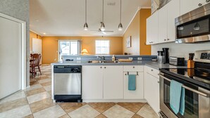 A modern kitchen with a dishwasher, oven, and stainless steel appliances. There is a dining area with a chair and table, and a window providing natural light. - 2BR Pet-friendly Vacation Rental The Villages! (Lady Lake)