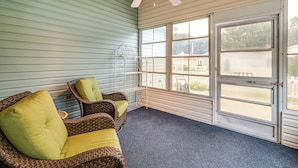 Ein Wintergarten mit Deckenventilator, Korbmöbeln und Blick auf einen weißen Zaun vor dem Haus.