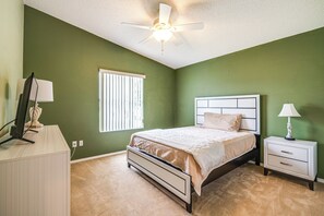 A bedroom with a bed, nightstand, lamp, ceiling fan, window with blinds, and a desk with a lamp. - 2BR Pet-friendly Vacation Rental The Villages! (Lady Lake)