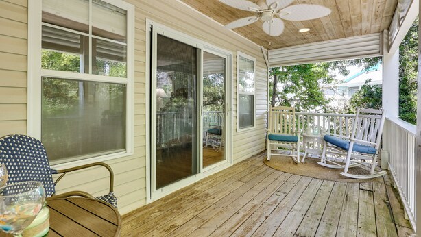 A covered porch with a ceiling fan, sliding glass doors, rocking chairs, and a table with chairs.