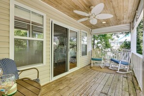 A covered porch with a ceiling fan, sliding glass doors, rocking chairs, and a table with chairs. - Steps to Ocean: Luxe Kure Beach Home w/ Game Room (Kure Beach)