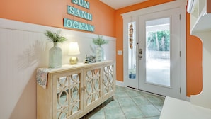 A hallway with an orange wall, a white door, and a decorative sign that reads "SUN, SAND, OCEAN".