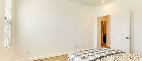 A bedroom with a bed, a red rug, a ceiling fan, and a door leading to another room.