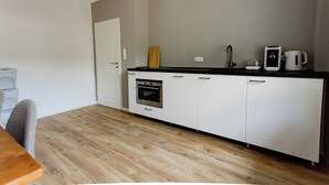 A compact kitchen with white cabinets, a built-in oven, a coffee maker, and a wooden cutting board on the countertop.