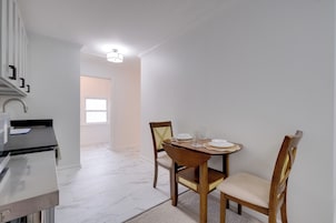 Uma sala de jantar com uma mesa posta para dois, bancada de cozinha e vista para outro ambiente.