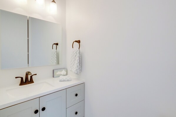 A bathroom with a white sink, a mirror, and two towels hanging on towel hooks.