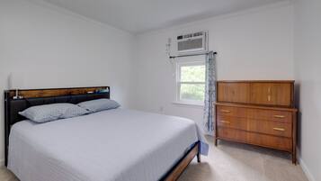 A bedroom with a bed, a wooden dresser, a window with curtains, and an air conditioning unit.