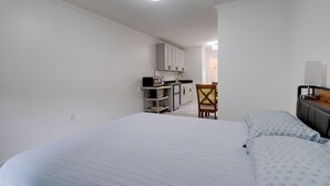 A bedroom with a bed, a chair, and a kitchenette in the background. - Dock Access: Waterfront Studio in Colonial Beach! (Colonial Beach)