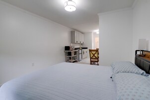 Quarto com cama, uma cadeira e uma cozinha compacta ao fundo.